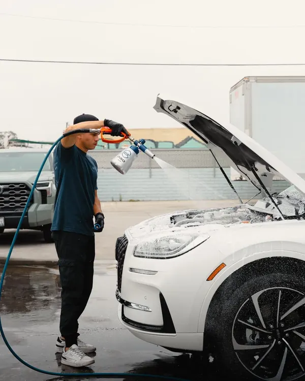 Detailer cleaning the engine bay of a white SUV