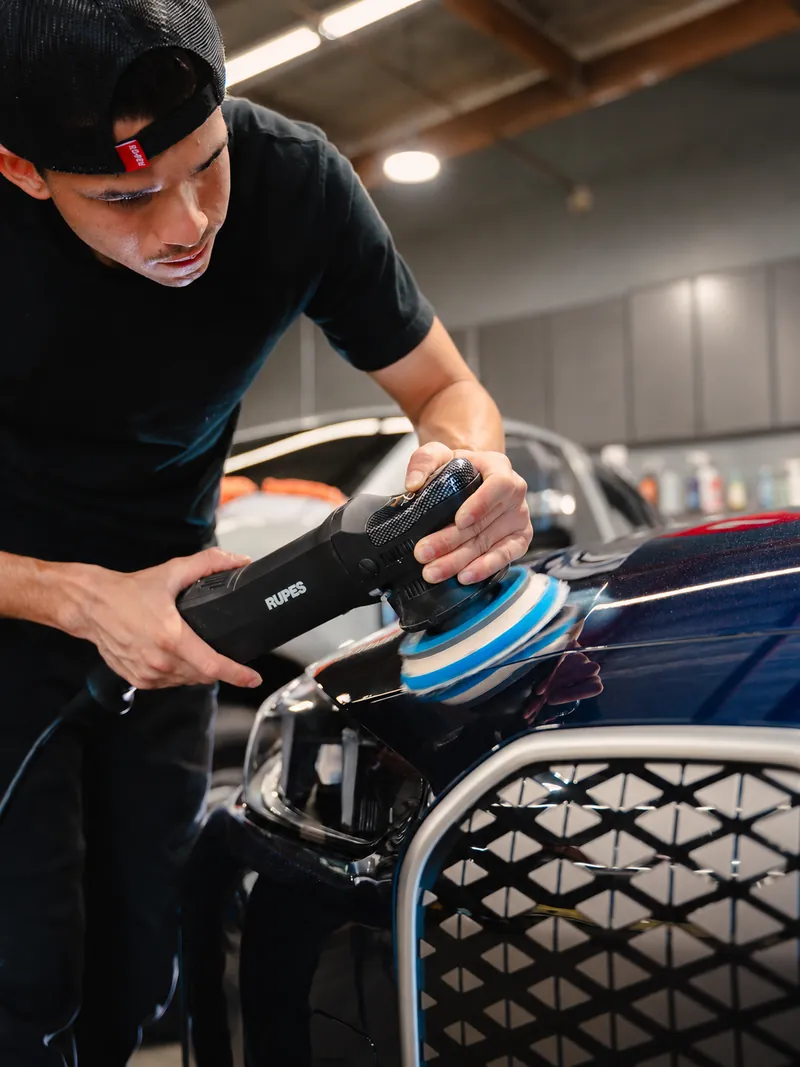Machine polishing a blue BMW with a dual-action polisher