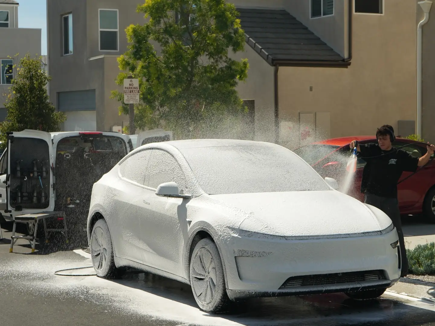 Our detailer foam-washing a white Tesla in a customer's driveway, with our work van parked beside it