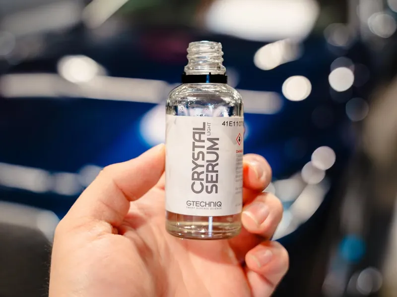 Bottle of ceramic coating held up in front of a blue car