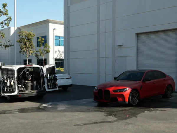 Red BMW M3 being detailed in an office parking lot, van open nearby