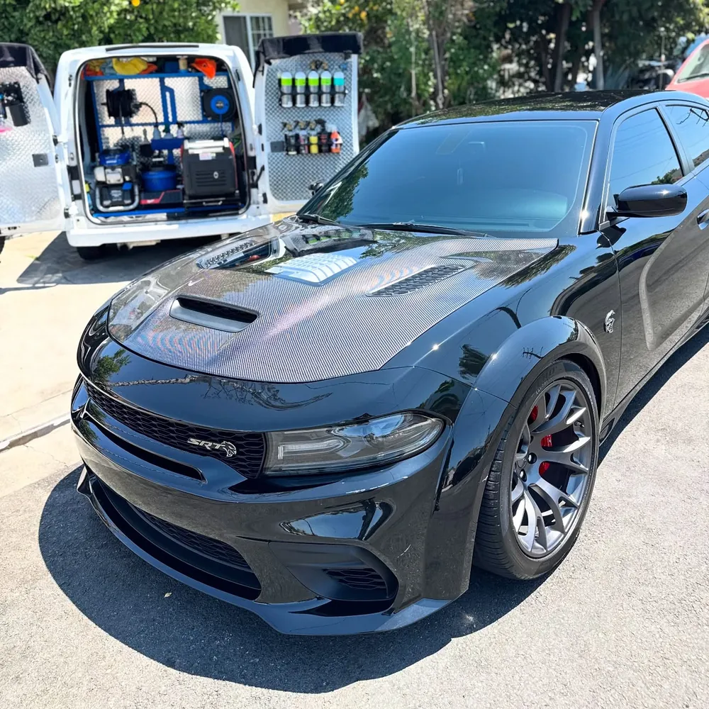 Our work van parked at a customer's home with the back doors open, next to a black Charger we just detailed
