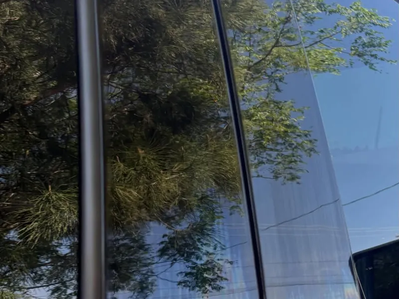 Glossy black door pillar reflecting trees and sky like a mirror