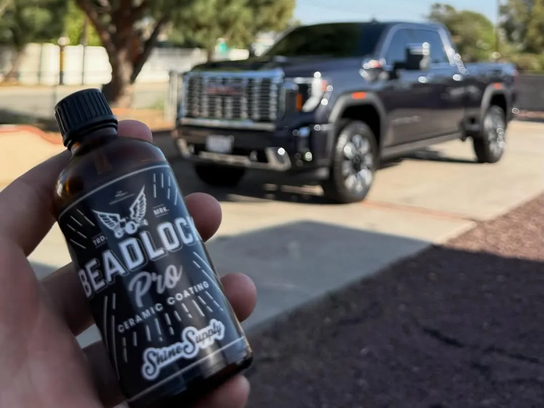 Ceramic coating bottle held up in front of a dark GMC Sierra Denali in a driveway