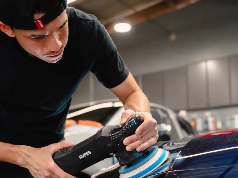 One of our detailers machine polishing a dark blue hood