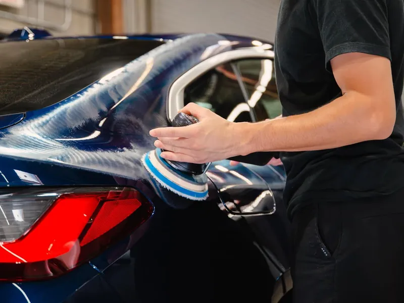Detailer polishing the rear quarter of a dark blue car