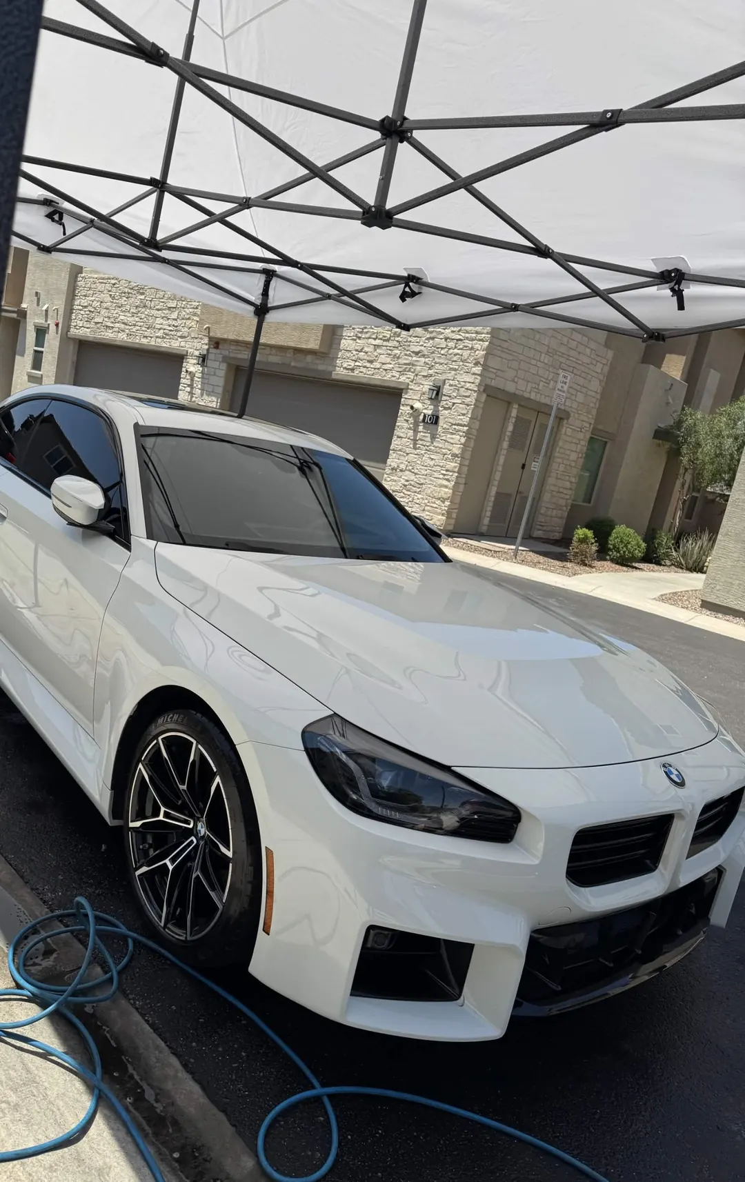 White BMW M2 being detailed under a white pop-up canopy