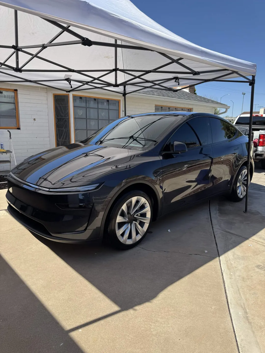Dark Tesla Model Y being detailed under a white pop-up canopy