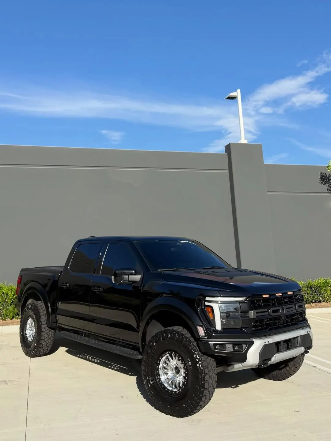 Black Ford Raptor on big tires parked in front of a gray wall