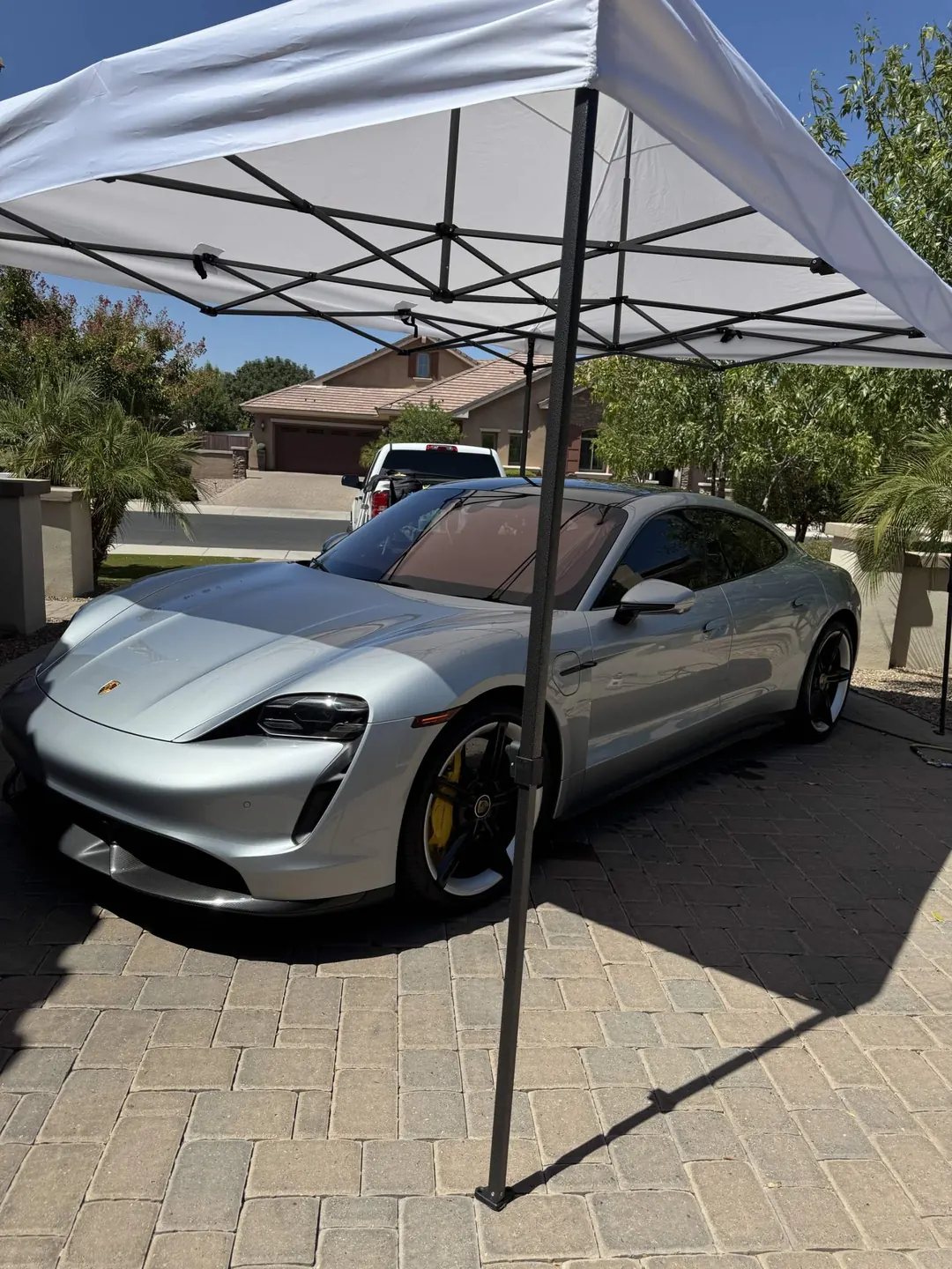 Silver Porsche Taycan being detailed under a white pop-up canopy